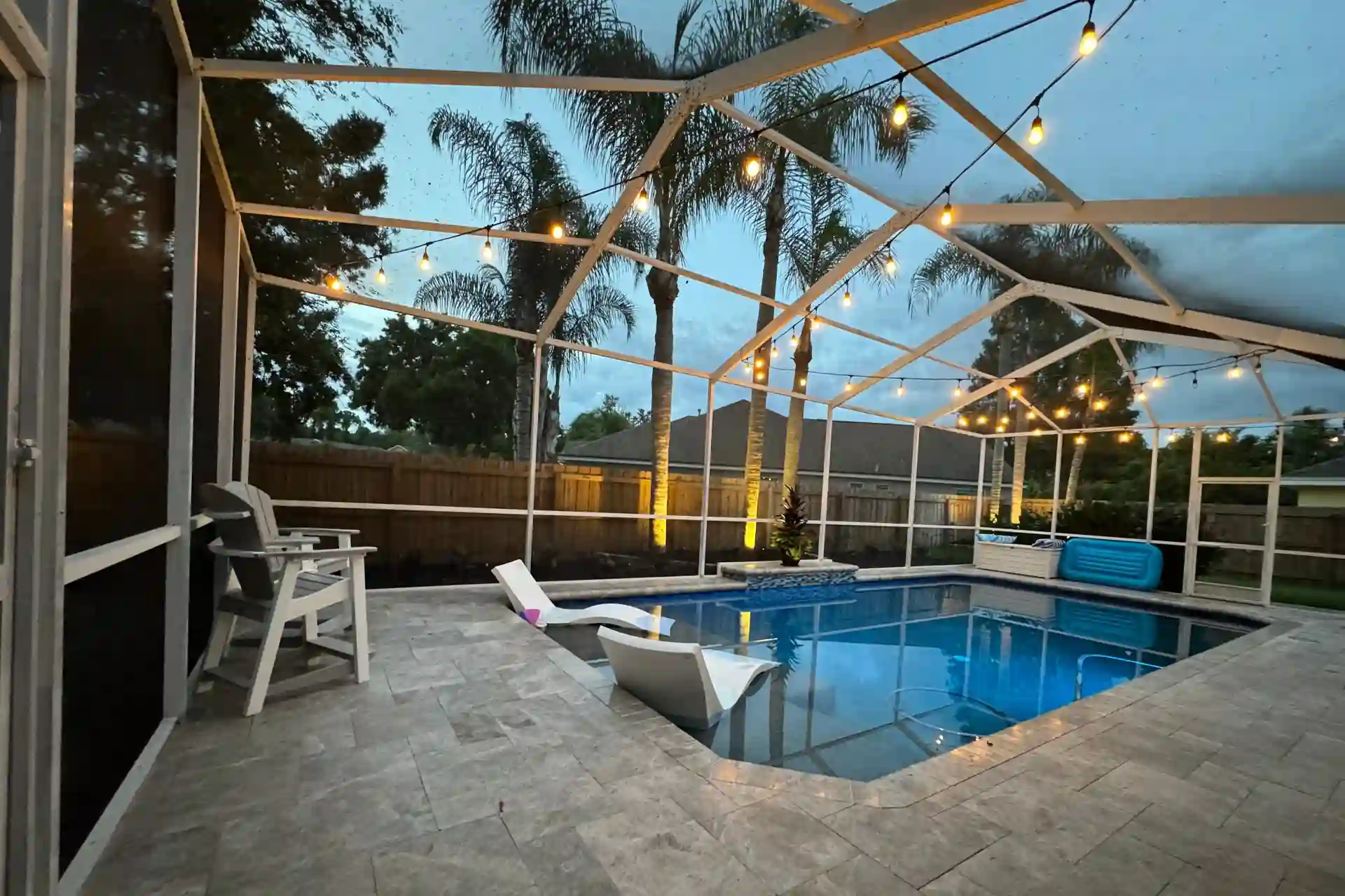 A screened pool enclosure at dusk with string lights overhead and palms visible through the screen
