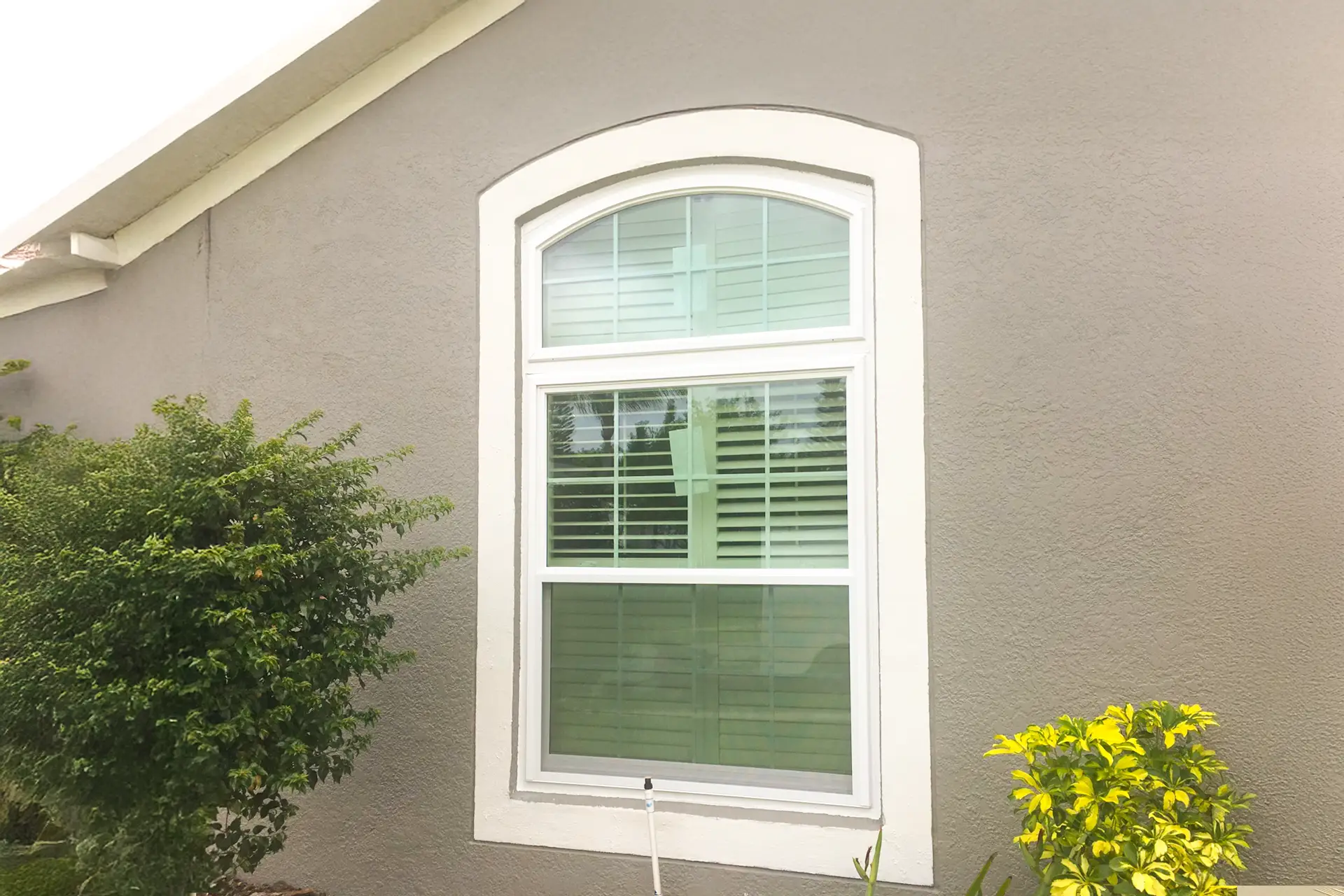A new white single-hung replacement window with an arched transom set into grey stucco, freshly sealed at the perimeter