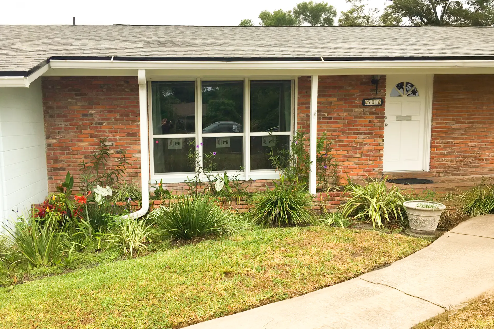 Front elevation of a red brick ranch home with a new white-framed picture window and flanking single-hung windows, factory labels still on the glass
