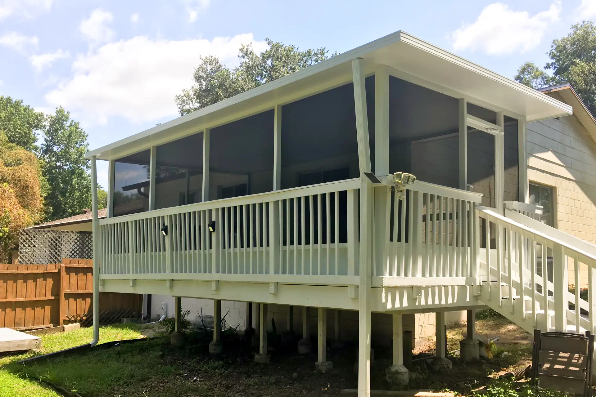 A screen room built onto an elevated deck with white railings at the back of a Central Florida house