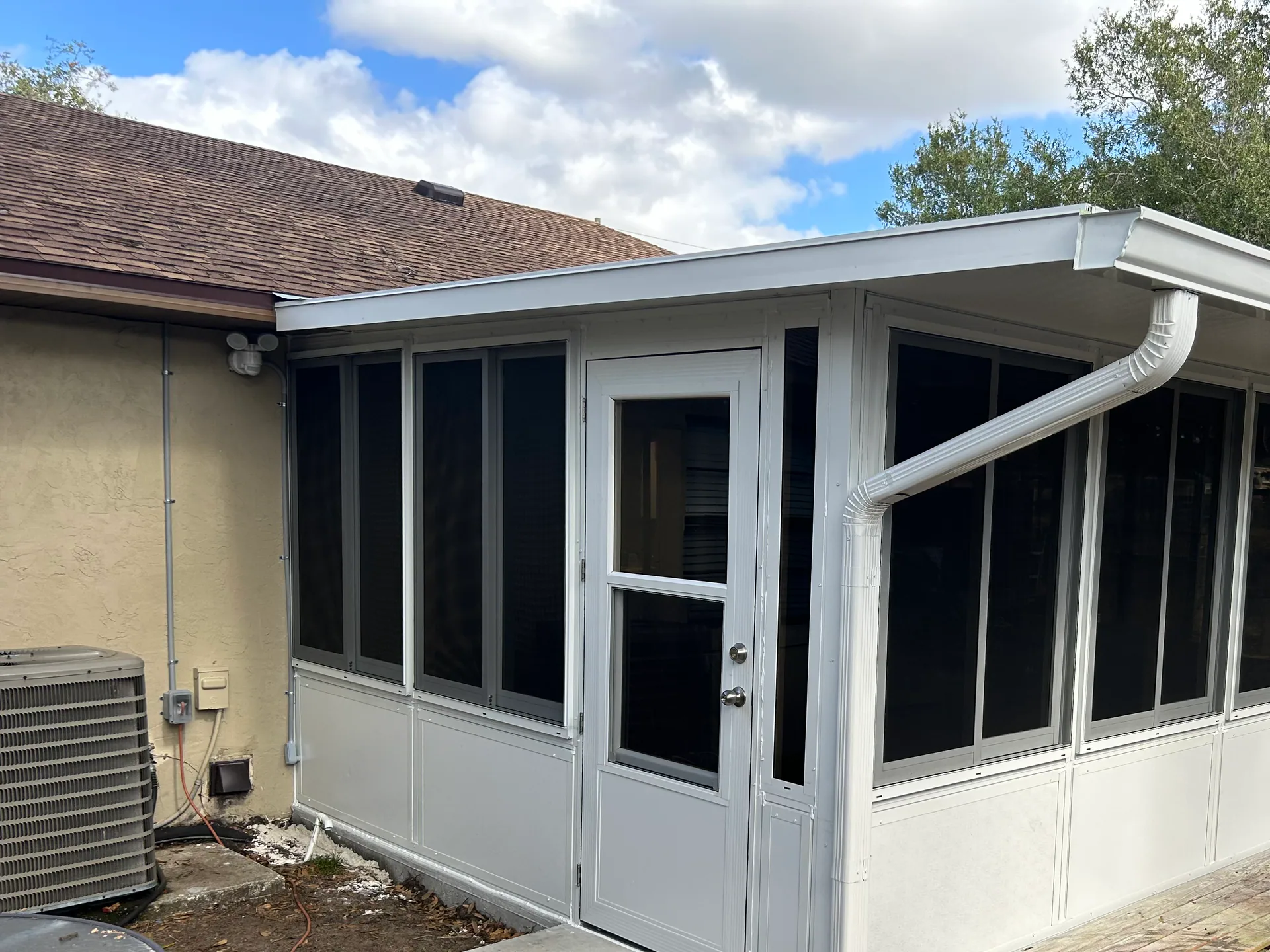 A white-framed screen room with dark screening, an entry door and integrated guttering attached to a Central Florida home