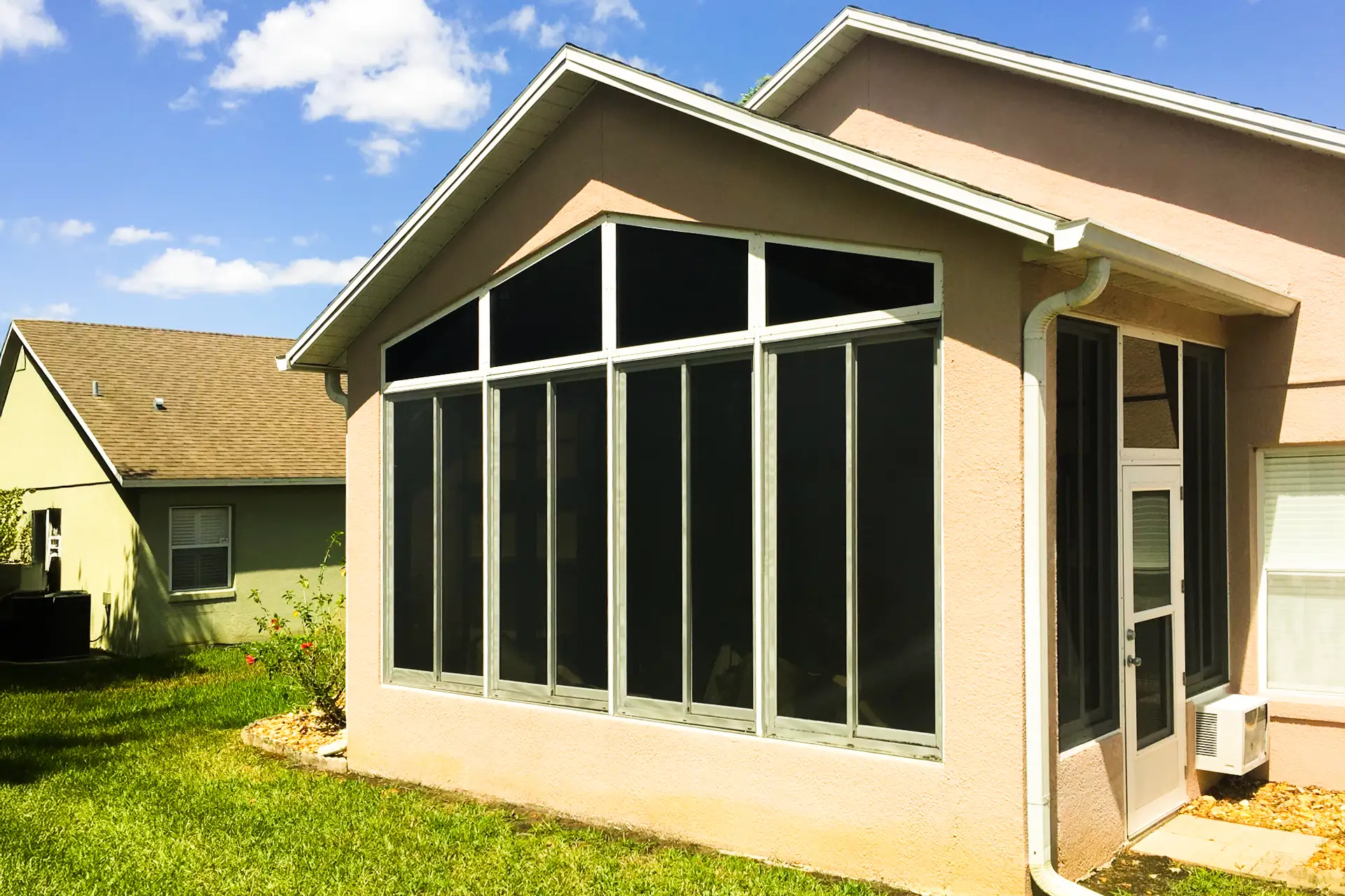 A gable-ended sunroom with white framing and tall glass panels added to the rear of a tan stucco Central Florida home